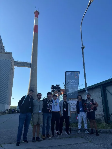 The RAICAM team standing in front of the Zwentendorf nuclear power plant's chimney next to the EnRicH 2025 hackathon banner